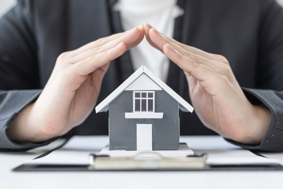 Home Protection Insurance Concept With Hands Over House
